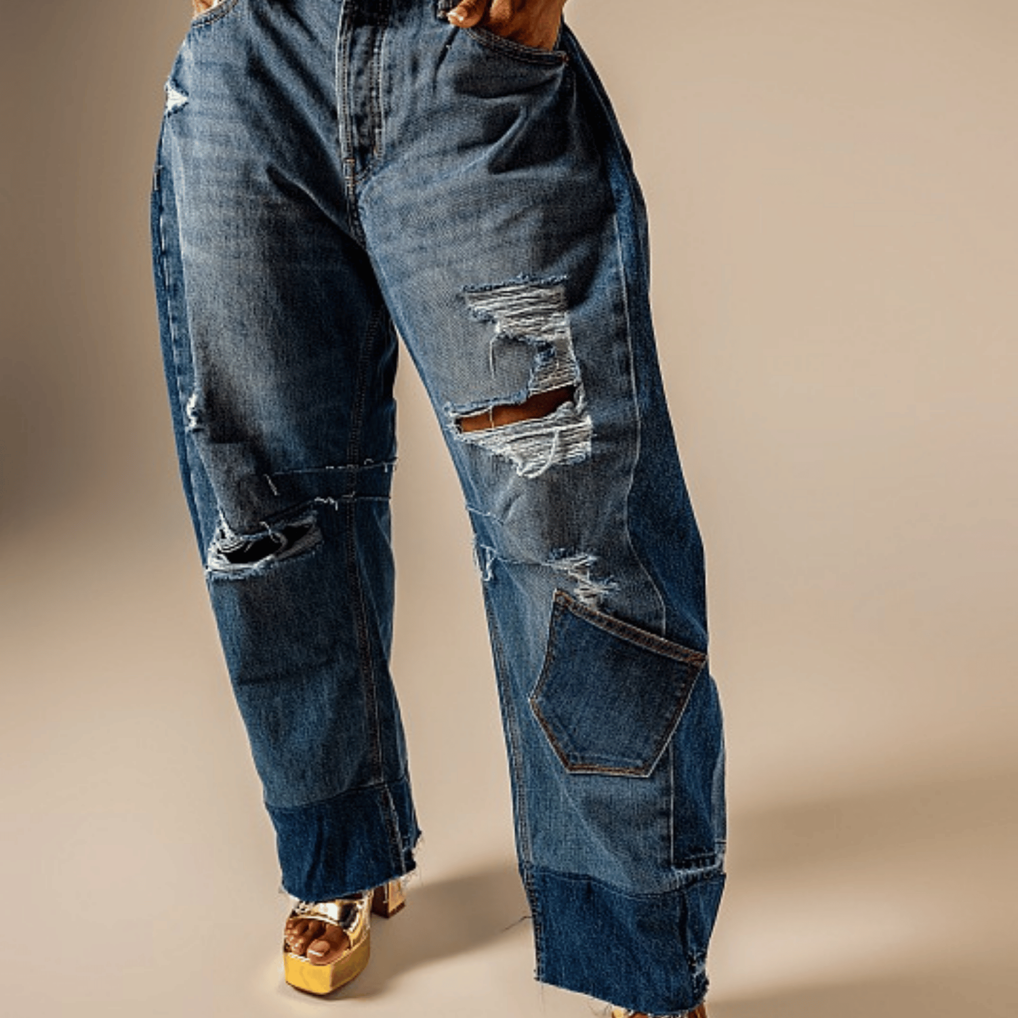 A person wearing distressed blue denim jeans with ripped details and large patch pockets, shown from the waist down against a plain beige studio background.