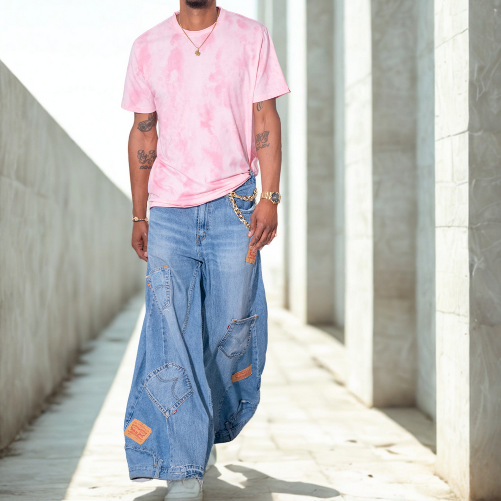 Person wearing a pink tie-dye shirt and blue patchwork palazzo jeans walking in a sunlit concrete area.