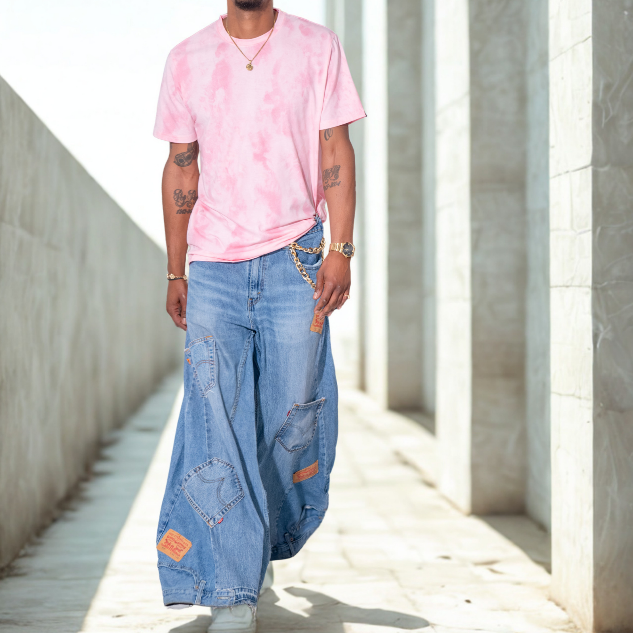 Person wearing a pink tie-dye shirt and blue patchwork palazzo jeans walking in a sunlit concrete area.
