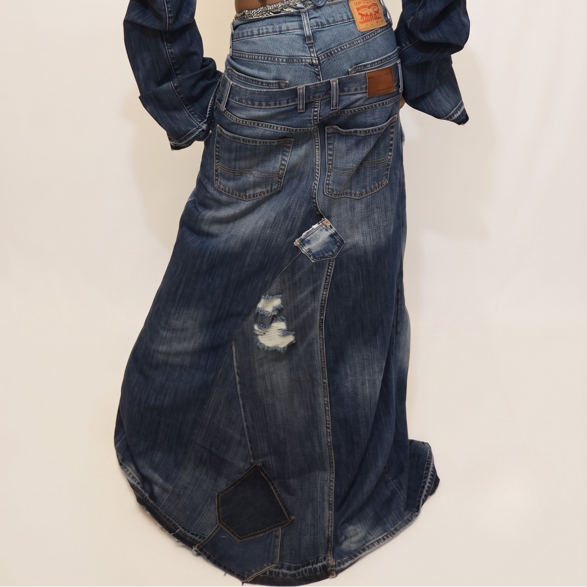 A model viewed from behind wearing a dark blue denim outfit consisting of a cropped long-sleeve top and a matching distressed denim skirt, set against a plain off-white studio background.